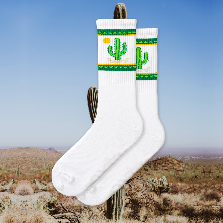 A pair of white socks with green and yellow cactus designs and a small cactus flower detail.