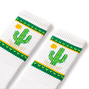 A pair of white socks with green and yellow cactus designs and a small cactus flower detail.