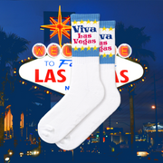 A pair of white socks with blue and yellow 'Viva Las Vegas' text and star patterns with Vegas sign in the background